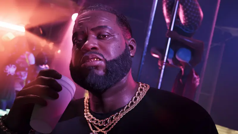 Boobie Ike in sunglasses and gold chains holds a cup inside a club