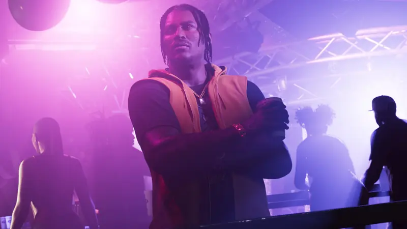 DreQuan Priest in an orange vest stands with crossed arms under purple club lights