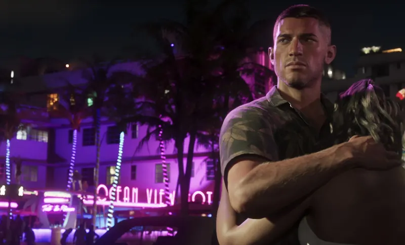 A man holds a woman close in front of the neon Ocean View hotel at night