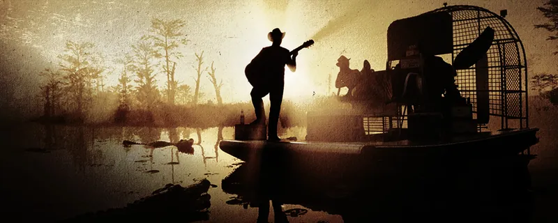 A silhouetted guitarist plays on an airboat in a misty swamp at sunrise