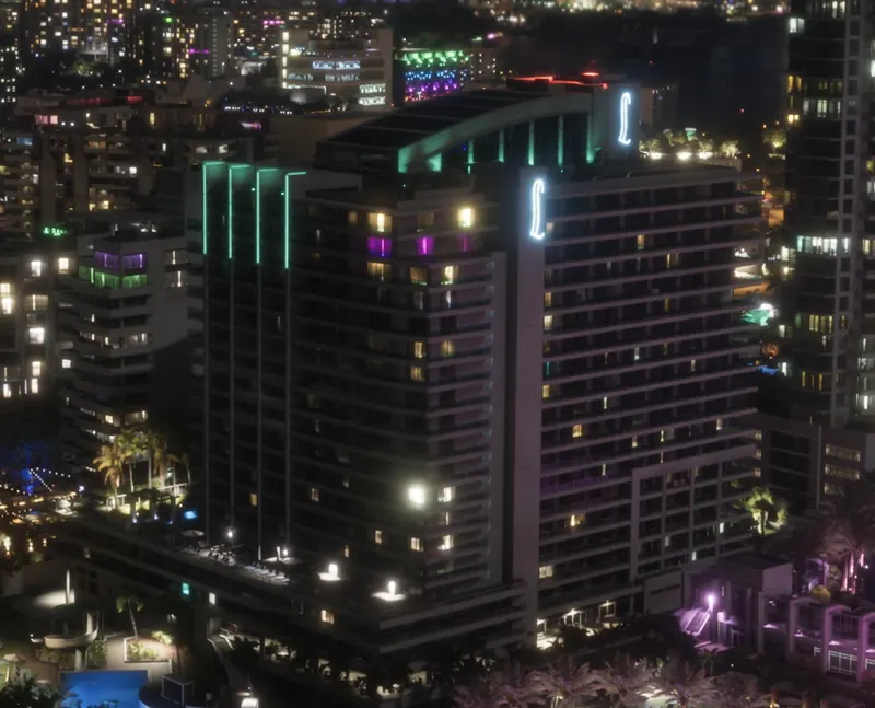 A Vice Beach hotel tower lit up in pink and green neon at night
