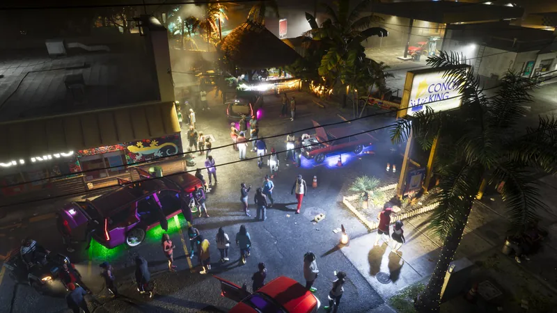 A busy street party with neon cars and crowds at night, seen from above